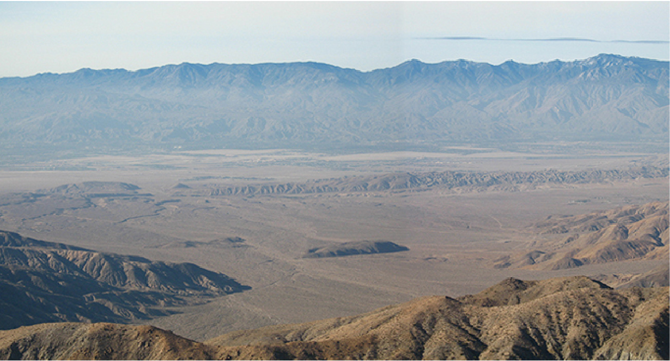 A photograph of a landscape showing mountains in the
distance, in the middle the land has a valley or series of hills:
it’s an earthquake fault. Further information is given in the caption.